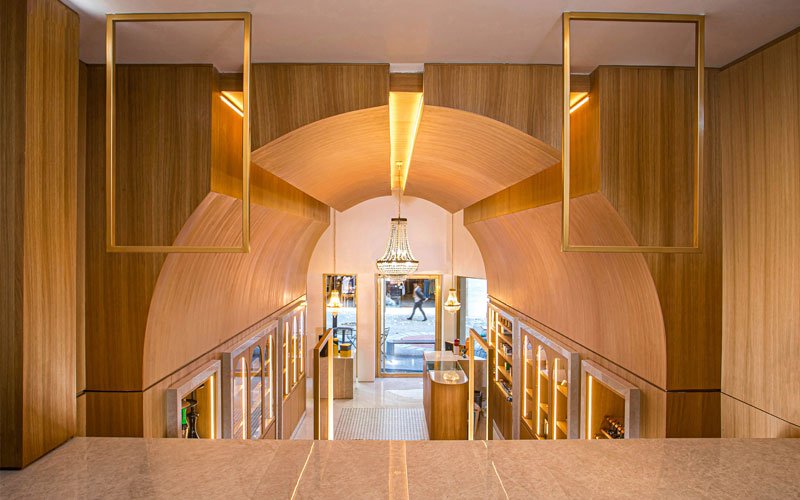 Interior view of a modern cigar shop featuring a curved wooden ceiling, elegant chandeliers, display cabinets with cigars, and warm ambient lighting