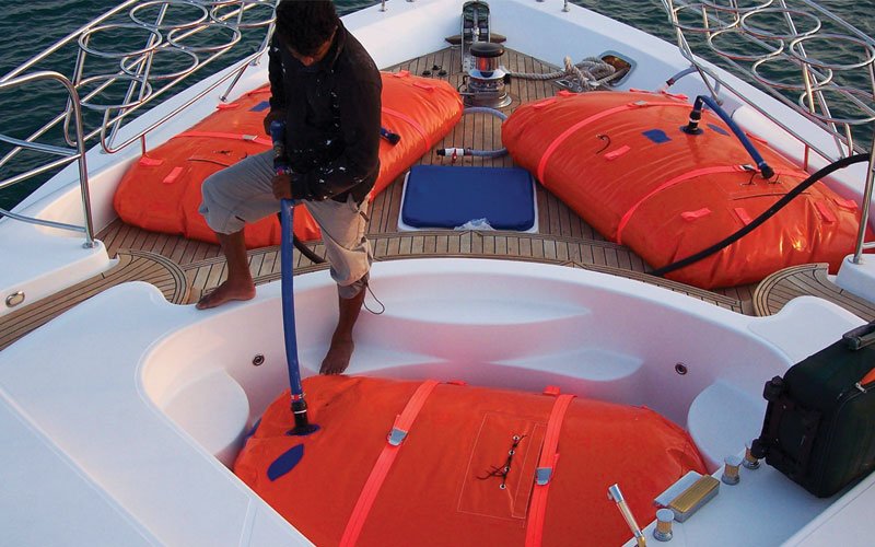 Sailing yacht equipped with Turtle-Pac flexible bladder tanks and liferaft gear, crew handling marine safety equipment during offshore sailing in rough seas and polar environments.