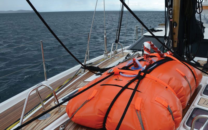 Sailing yacht equipped with Turtle-Pac flexible bladder tanks and liferaft gear, crew handling marine safety equipment during offshore sailing in rough seas and polar environments.