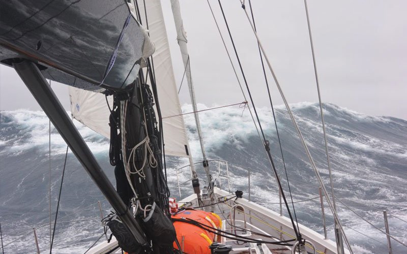 Sailing yacht equipped with Turtle-Pac flexible bladder tanks and liferaft gear, crew handling marine safety equipment during offshore sailing in rough seas and polar environments.