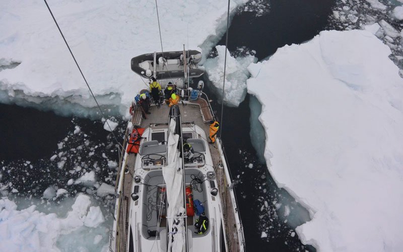 Sailing yacht equipped with Turtle-Pac flexible bladder tanks and liferaft gear, crew handling marine safety equipment during offshore sailing in rough seas and polar environments.