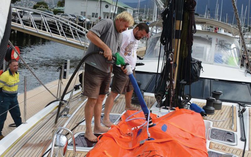 Sailing yacht equipped with Turtle-Pac flexible bladder tanks and liferaft gear, crew handling marine safety equipment during offshore sailing in rough seas and polar environments.