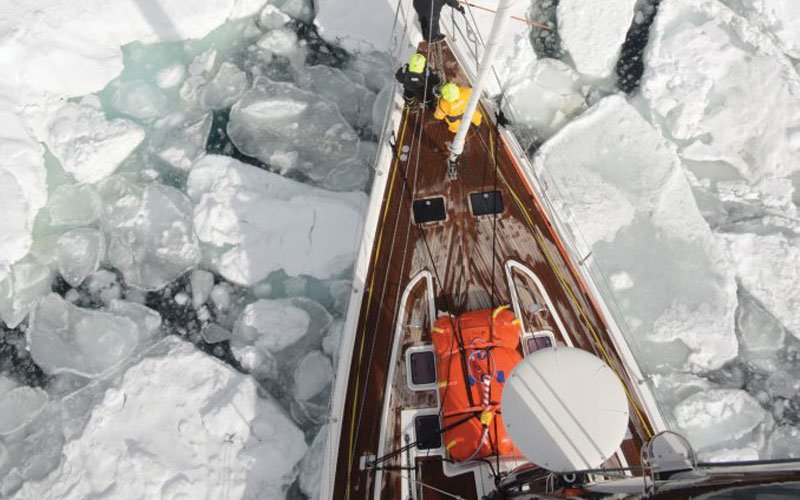 Sailing yacht equipped with Turtle-Pac flexible bladder tanks and liferaft gear, crew handling marine safety equipment during offshore sailing in rough seas and polar environments.