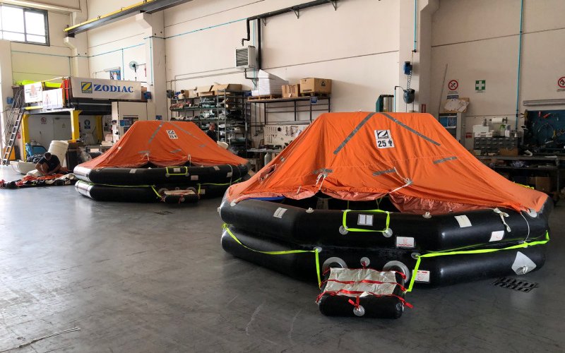 The Versilia Marine Service storage and maintenance facility, featuring two polygonal inflatable lifeboats. Metal shelves stocked with supplies and a well-organized workspace are visible in the background