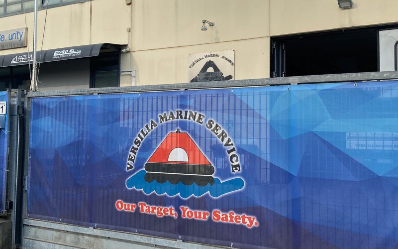 A blue banner with the Versilia Marine Service logo standing in front of a building