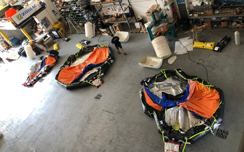 The Versilia Marine Service storage and maintenance facility, featuring three deflated polygonal inflatable lifeboats. A staff member, seen from behind, is working in the space, surrounded by various equipment and supplies
