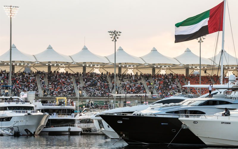 Luxury yachts docked at Yas Marina with a large UAE flag and grandstand seating in the background.