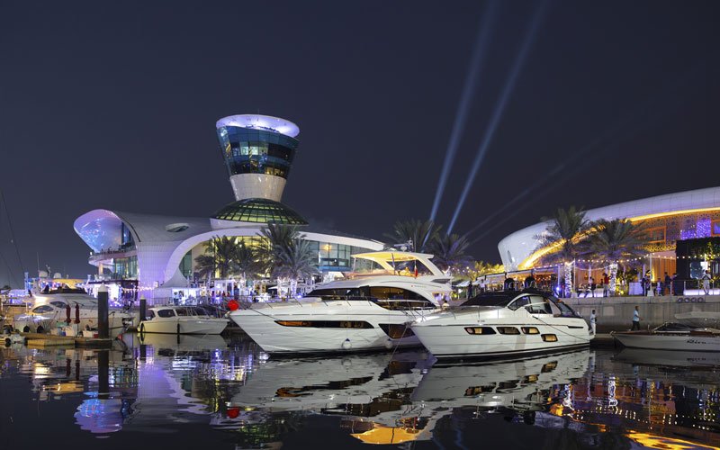 Night view of Yas Marina with colorful lights reflecting on the water and yachts docked along the promenade.