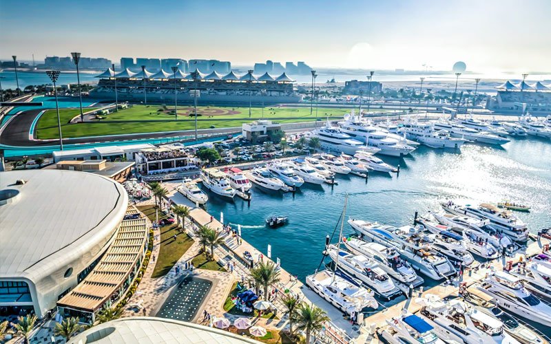 Panoramic daytime view of Yas Marina filled with yachts beside the Formula 1 circuit and grandstands.