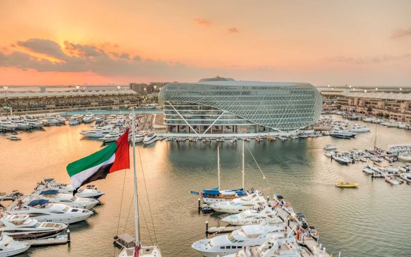 Sunset view over Yas Marina with yachts, the Yas hotel structure, and a UAE flag overlooking the water.