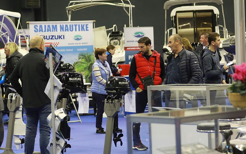 Indoor scene from the Zagreb Boat Show showcasing various RIBs, marine engines and equipment on display. Attendees are seen interacting with exhibitors, examining the equipment and their features.