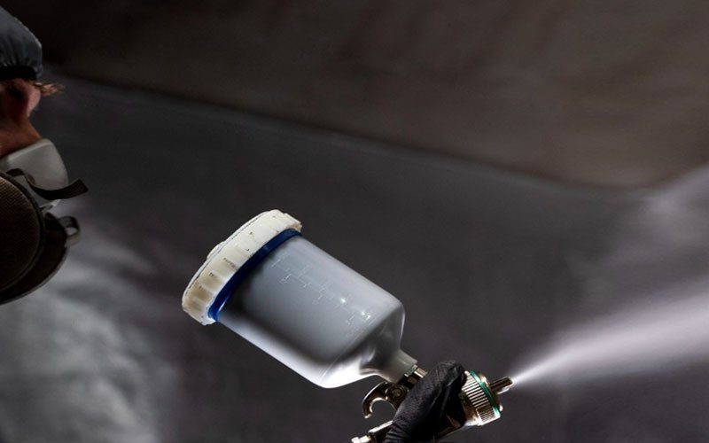 A technician wearing a protective suit and specialized mask is spray-painting a yacht using a spray gun, focusing on precision and even coverage