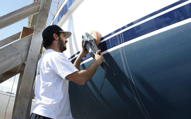 A technician is using a specialized electric brush to clean and polish the yacht's paint, focusing on achieving a smooth and glossy finish
